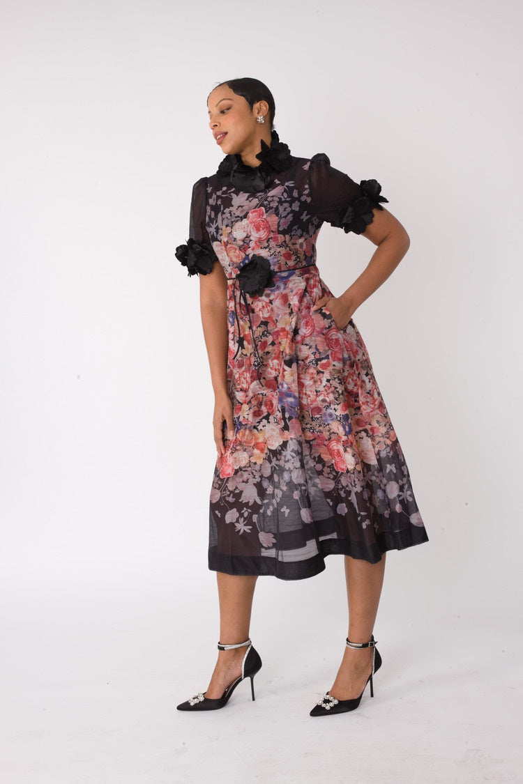 Model wearing the black multi romantic floral midi dress with hands on hips, highlighting statement floral appliqué sleeves and flowing midi silhouette by For Her NYC