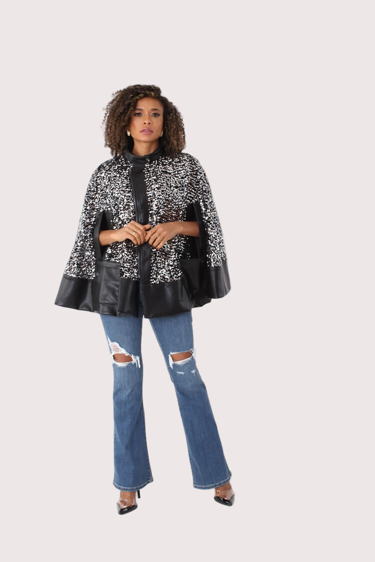 Front view of black sequin embellished cape with faux leather trim, styled over jeans — For Her NYC.