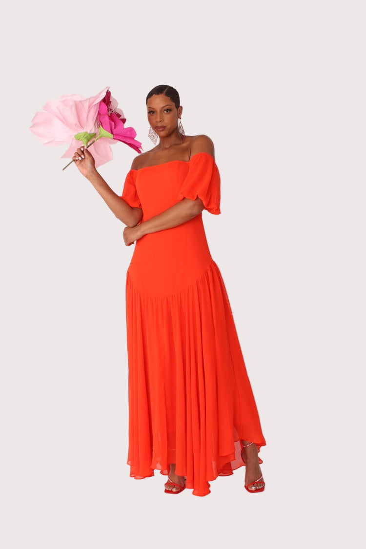 Red off-shoulder maxi dress shown front view with arm raised pose, flowing ruffle detail, For Her NYC