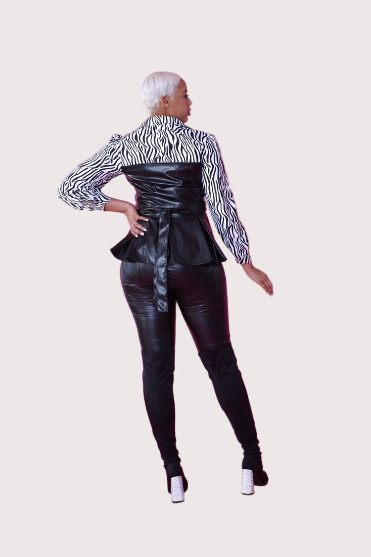 Angled view of black and white zebra print peplum top with faux leather bodice, hand on hip – For Her NYC